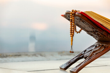 A serene moment of faith. A Quran and prayer beads rest against a backdrop of a tranquil nature scene, with a minaret subtly placed in the distance.