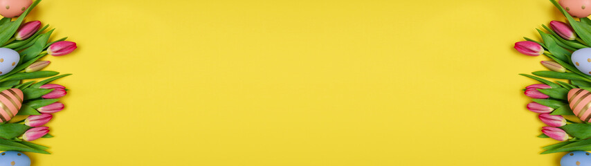 Easter background with colorful eggs and spring flowers on yellow background with copy space, top view