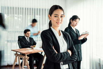 Portrait of happy young asian businesswoman looking at camera with motion blur background of business people movement in dynamic business meeting. Habiliment