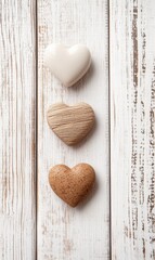 Fototapeta premium Three heart-shaped stones rest gently on a white wooden table, exuding a timeless charm perfect for celebrating love on Valentine's Day.