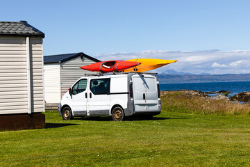old beater of a van parked on grass with two canoes or kayaks strapped / secured to the roof rack on a sunny day, © Sven