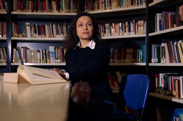 Woman reading in a library surrounded by bookshelves during study time