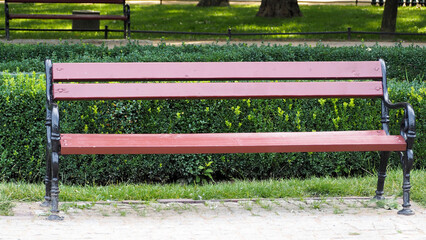 A brown bench with a backrest stands in a park against the background of green grass on a summer day