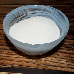 white sugar crystals in blue glass plate on brown wooden background. side view. copy space