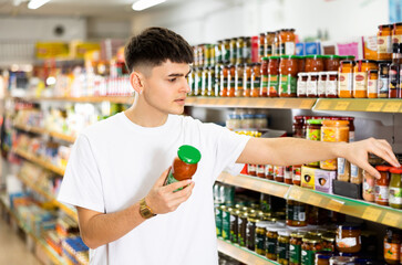 Young male customer diligently picking out tomato paste