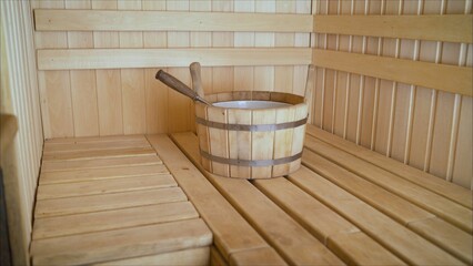 Wooden bucket with metal rings and a ladle inside a sauna made of light wood, ready for a relaxing experience