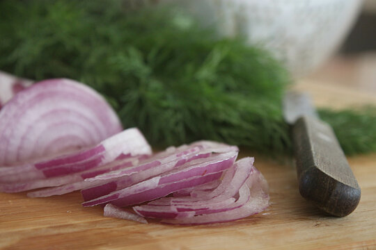 Close-up of Sliced red onions and dill on a wooden chopping board