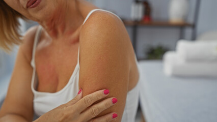 Middle age woman with blond hair and pink nails touches arm in relaxing spa room for wellness and beauty treatment