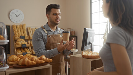 Man serving a woman coffee in a bakery with bread and pastries on display, highlighting the friendly customer service in an indoor shop setting