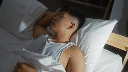 Young, handsome, asian man sleeping peacefully on a white pillow in a cozy bedroom, capturing a...