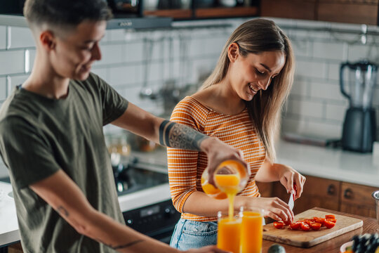 Lesbian couple preparing breakfast with orange juice and tomatoes in modern kitchen