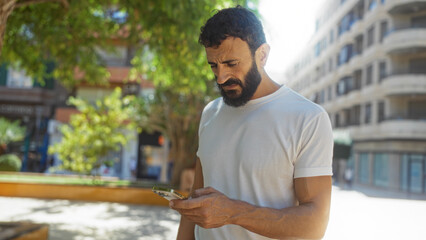Handsome hispanic man using smartphone outdoors in urban park on sunny day