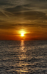 Shiny dramatic sunset with many chemical trails on the sky above wavy sea surface