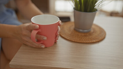 Woman holding coffee cup in cozy cafe setting with indoor plant and wicker coaster on wooden table