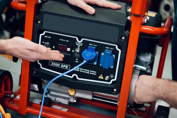 Close up. Salesman in red shirt and baseball cap is showing couple of clients new generator in power tools store.