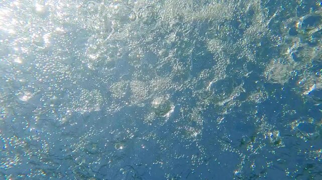 Raindrops dripping on a turquoise water surface on a sunny day against a blue sky background, Backlighting (Contre-jour) Underwater shot, Slow motion