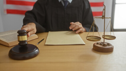 Judge in courtroom with gavel and scales of justice on wooden desk with american flag in background