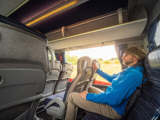 Male tourist in green hat and blue jacket on back sit of a bus. Man on a journey. Travel and tourism industry. Person enjoy long ride.