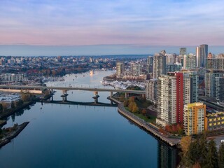 Obraz premium Aerial view of Vancouver city skyline, waterfront, and bridge. Modern high-rise buildings reflect on calm water. Boats in marina. Downtown, Vancouver, British Columbia, Canada