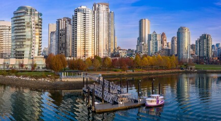 Fototapeta premium Colorful ferry approaches dock in Vancouver city. Autumn colors reflect on the water. Yaletown, Vancouver, British Columbia, Canada