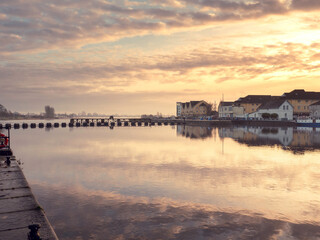 Obraz premium Athlone city riverside at warm sunset. Cloudy sky reflects in river Shannon. Popular old town, shopping, educational and industrial center. Tourist and travel hub.