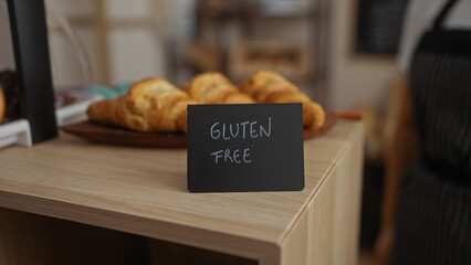 Gluten free sign in a bakery shop with croissants on a wooden counter in the background.
