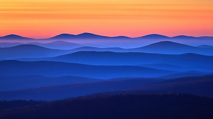 Obraz premium Serene sunset over rolling blue mountains with soft hues and distant silhouettes in the background