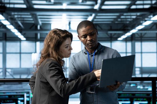 Computer scientists in data center using notebook, integrating green technologies. African american man and colleague in server room implementing sustainable energy solutions