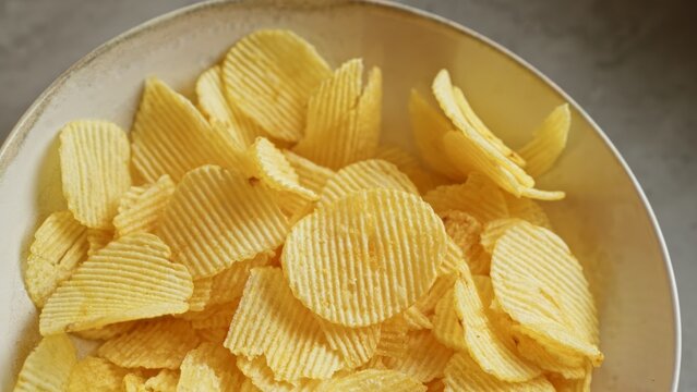 Closeup showing a bowl of crispy potato chips placed on a smooth concrete surface depicting a casual snack setting