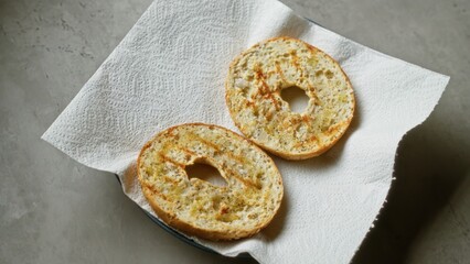 Toasted bagel halves sitting on a paper towel over a concrete surface, highlighting their golden texture and crispy edges.