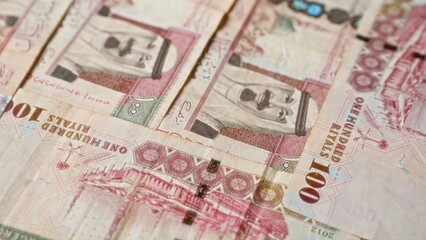Saudi arabian banknotes in denominations of 100 riyals are closely arranged, highlighting the intricate details and designs on the currency.