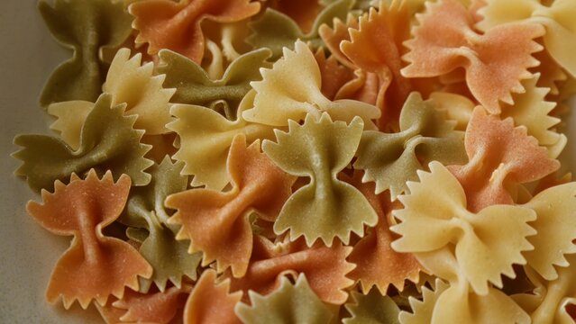 Closeup showing colorful farfalle pasta in various shades of orange, green, and beige, highlighting the beautiful texture and pattern of the bowtie-shaped noodles enhancing their culinary appeal.