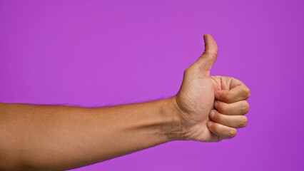 Man's hand giving a thumbs-up gesture against a vibrant purple background, showcasing positivity...