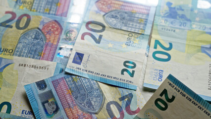 Euro banknotes scattered on a surface showcasing various twenty euros bills from the european union with detailed designs and holograms.