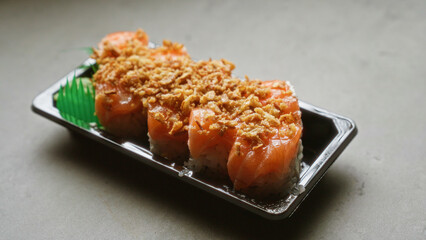 Delicious sushi roll with crispy toppings in a plastic tray under natural light on a minimalist table surface