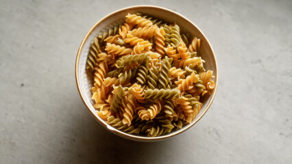 Bowl filled with colorful spiral pasta on a gray concrete surface in kitchen setting