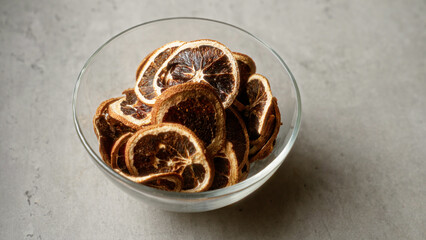 Bowl filled with dried citrus slices sitting on a grey concrete surface in bright light creating a minimalist still life photo ideal for healthy snacking or culinary ingredients
