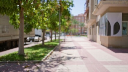 Obraz premium Out-of-focus outdoor scene featuring blurred trees, street, and buildings in the background with bokeh effect on a sunny day.