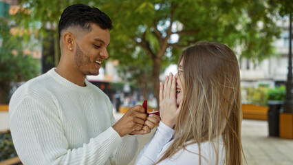 Man proposing to woman in an outdoor park setting, surrounded by urban cityscape, showcasing a romantic moment of love and engagement in a beautiful town environment.