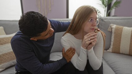 Woman and man sitting on sofa at home, expressing emotions and relationship dynamics in a modern apartment setting, with thoughtful expressions and cozy interior.