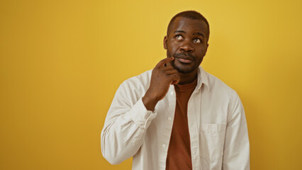 Obraz premium Handsome young african american man in white shirt and thoughtful pose over isolated yellow background