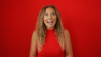 Surprised blonde hispanic woman over isolated red background, conveying astonishment and excitement.