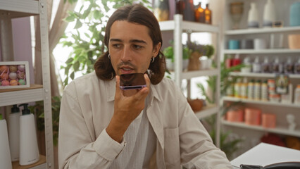 Fototapeta premium Young hispanic man with long hair speaks into a cellphone in a well-decorated home decor store surrounded by various indoor decorations.