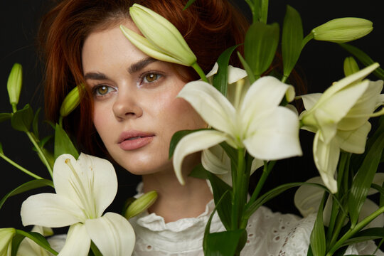 A beautiful portrait of a young woman with red hair surrounded by white lilies, conveying serenity and elegance in a soft spring atmosphere