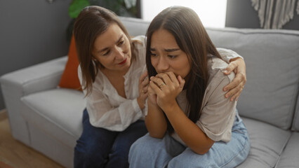 Woman comforting upset daughter on sofa in living room showing family, love, and support at home, highlighting adult, people, and interior setting in apartment.