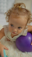 Fototapeta premium Toddler girl with blonde hair playing with a purple ball in a cozy bedroom setting illustrating cute childhood moments indoors