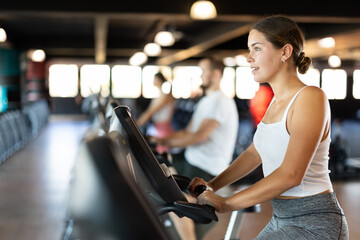 Fototapeta premium Young woman in sportswear training on exercise bike in gym