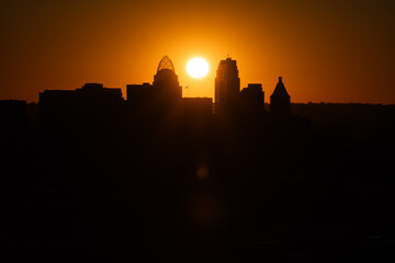 Sunrise over Cincinnati downtown city skyline with silhouettes of buildings and warm orange hues