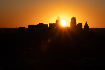 Sunrise over Cincinnati downtown city skyline with silhouettes of buildings and warm orange hues