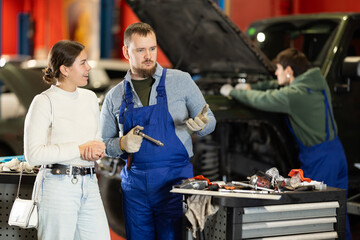 Auto mechanic checking young woman client car in car service center